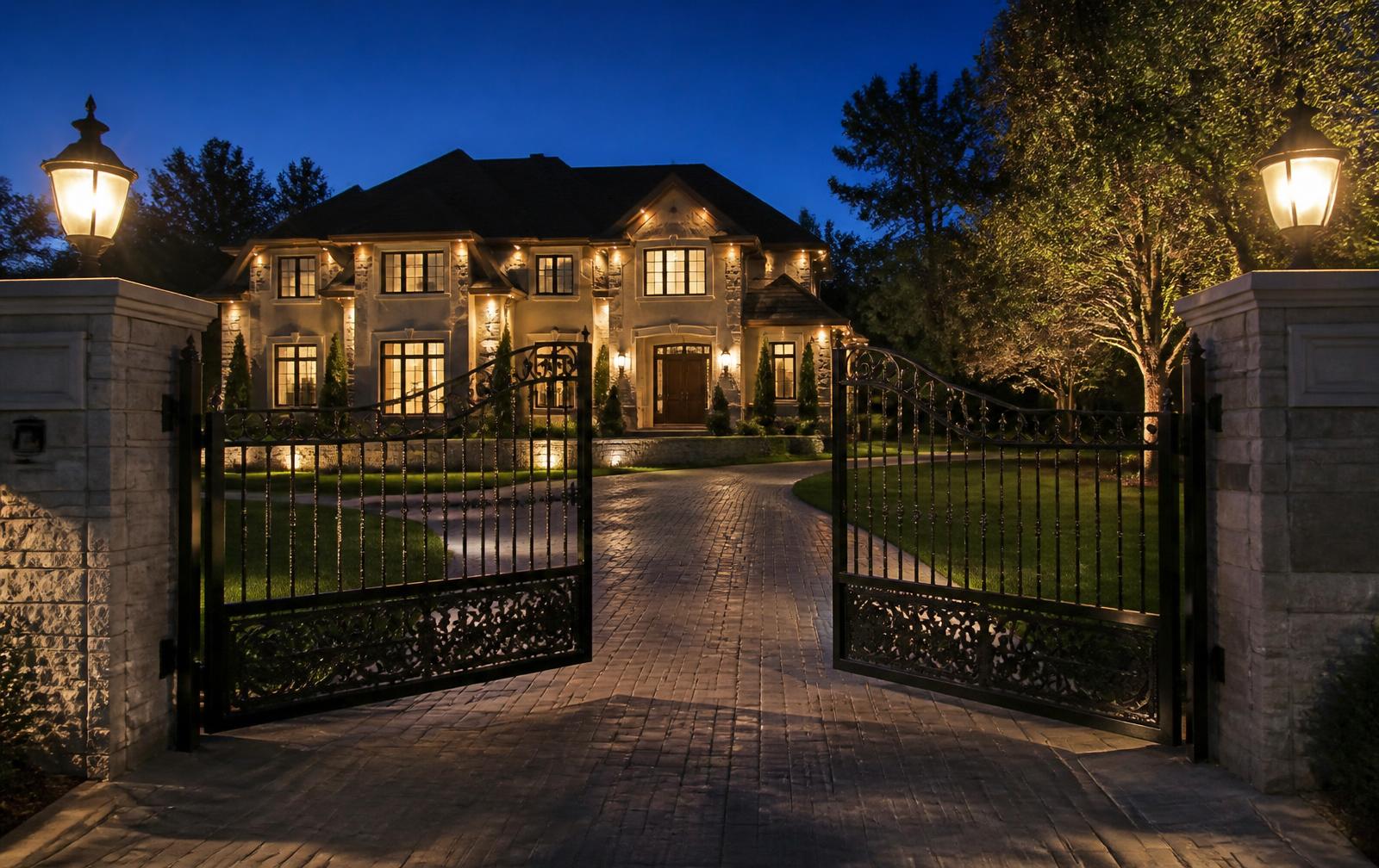 Automatic wrought-iron driveway gate opening in front of an upscale home at dusk